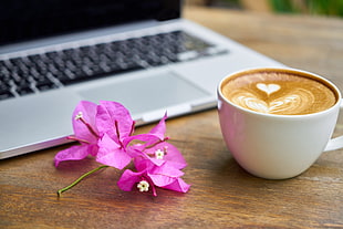 purple petaled flower beside cup of coffee and laptop computer on brown wooden table