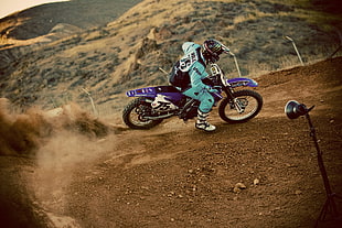 man wearing teal motocross jacket riding and driving blue dirt bike at daytime