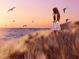 woman in black and white sleeveless midi dress in front of ocean surrounded of birds during sunset
