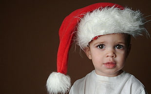 baby in white shirt wearing white and red Santa Claus hat