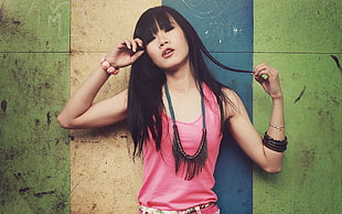 woman in pink scoop-neck tank top and black and blue necklace stands near green, blue, and yellow painted wall