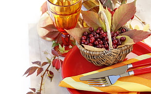red fruits on brown wicker basket near amber footed drinking glass and stainless steel fork