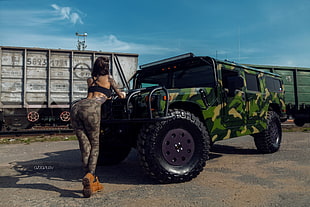 woman in brown camouflage pants standing infront of green camouflage Hummer H1