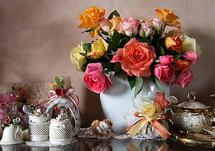 close up photo of bouquet of assorted color roses on white ceramic vase near the canisters