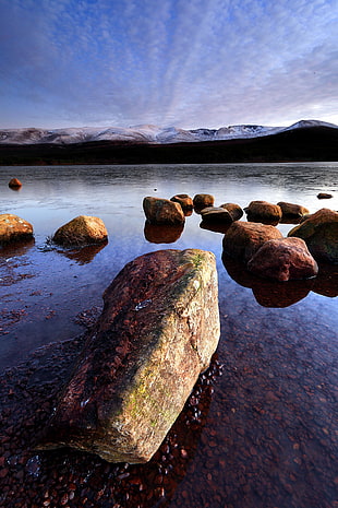 landscape photo of river and rocks under white cloud blue skies, loch morlich, highlands, scotland