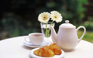 ceramic teapot beside teacup and two croissant breads on saucer