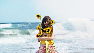 woman carrying sunflowers near sea