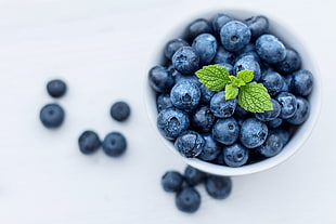 selective focus photography of blue berries on white ceramic cup