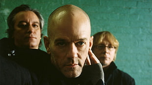 three men wearing black stands near green wall
