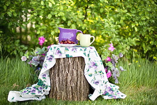 purple and white ceramic mug on floral coat on wood log
