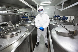person wearing white laboratory suit between gray containers
