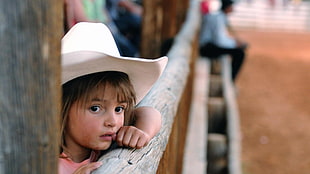 girl in white cowboy hat leaning towards gray log fence