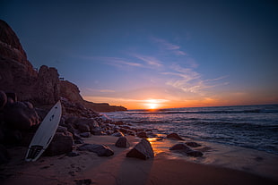 white surfboard leaning on rock near water at sunset