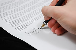 person holding ink pen signing on printer paper