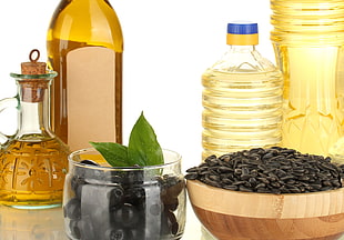 black olives on clear glass jar beside sunflower seeds and four olive oil and sunflower seed oil bottles