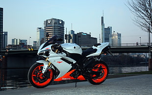 white and red Yamaha R1 near body of water in distant of high rise buildings