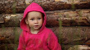 boy wearing pink hoodie beside brown wooden logs