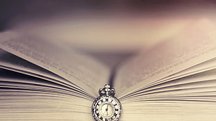 round silver-colored pocket watch on top of book page