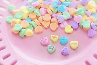 close up image of heart-shaped pink, green, blue, and orange candies on pink plate