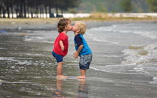 selective focus photography of boy and girl kissing on seashore line