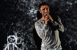 man swearing grey sweatshirt holding wireless microphone with black background