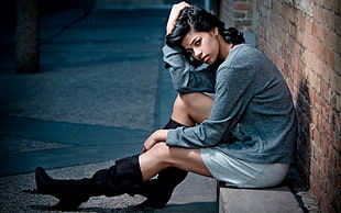 woman in gray long-sleeved shirt sitting on concrete brick near on wall bricks