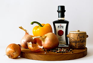 still-life photo of onions, bell pepper, Fini bottle and brown canister on brown wooden surface
