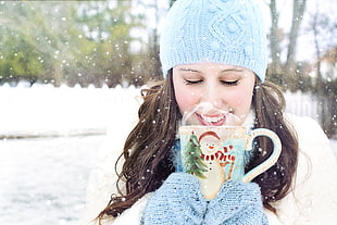 selected focus photo of a woman wearing winter jacket and gloves holding snowman embossed ceramic mug while smiling