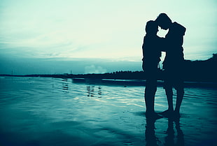 couple standing on body of water during sunset