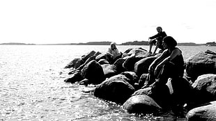 thee man sitting on gray stones near body of water