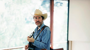men's blue chambray jacket holding guitar and wearing beige cowboy hat