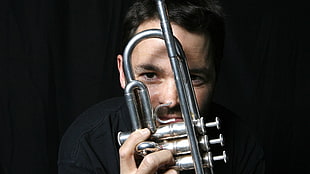 black haired man in black shirt holding trumpet