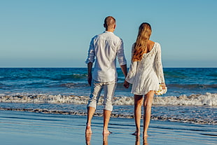 man and woman holding hands on seashore during daytime HD wallpaper