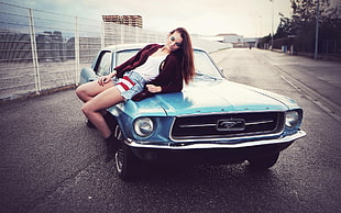 woman sitting on classic blue Ford Mustang coupe
