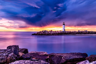 panoramic photography of white lighthouse surrounded by body of water under gray sky during golden hour