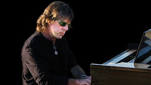 man wears black elbow sleeve shirt and black sunglasses plays piano