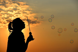 silhouette of woman blowing bubbles during sunset