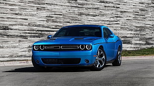 blue Dodge Charge parked on gray cement pavement beside gray wall