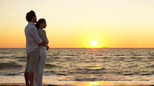 couple embracing each other near body of water during sunset