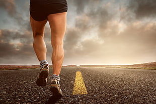 man wearing black shorts and gray running shoes on black road pavement HD wallpaper