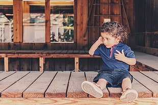 boy sitting on brown wooden flooring while holding his right ear