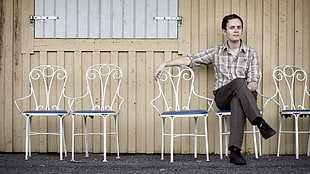 man sitting on one of five white metal armchairs