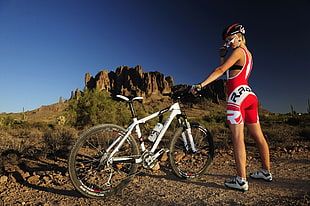 woman in red and white cycling clothes holding white hard-tail bicycle