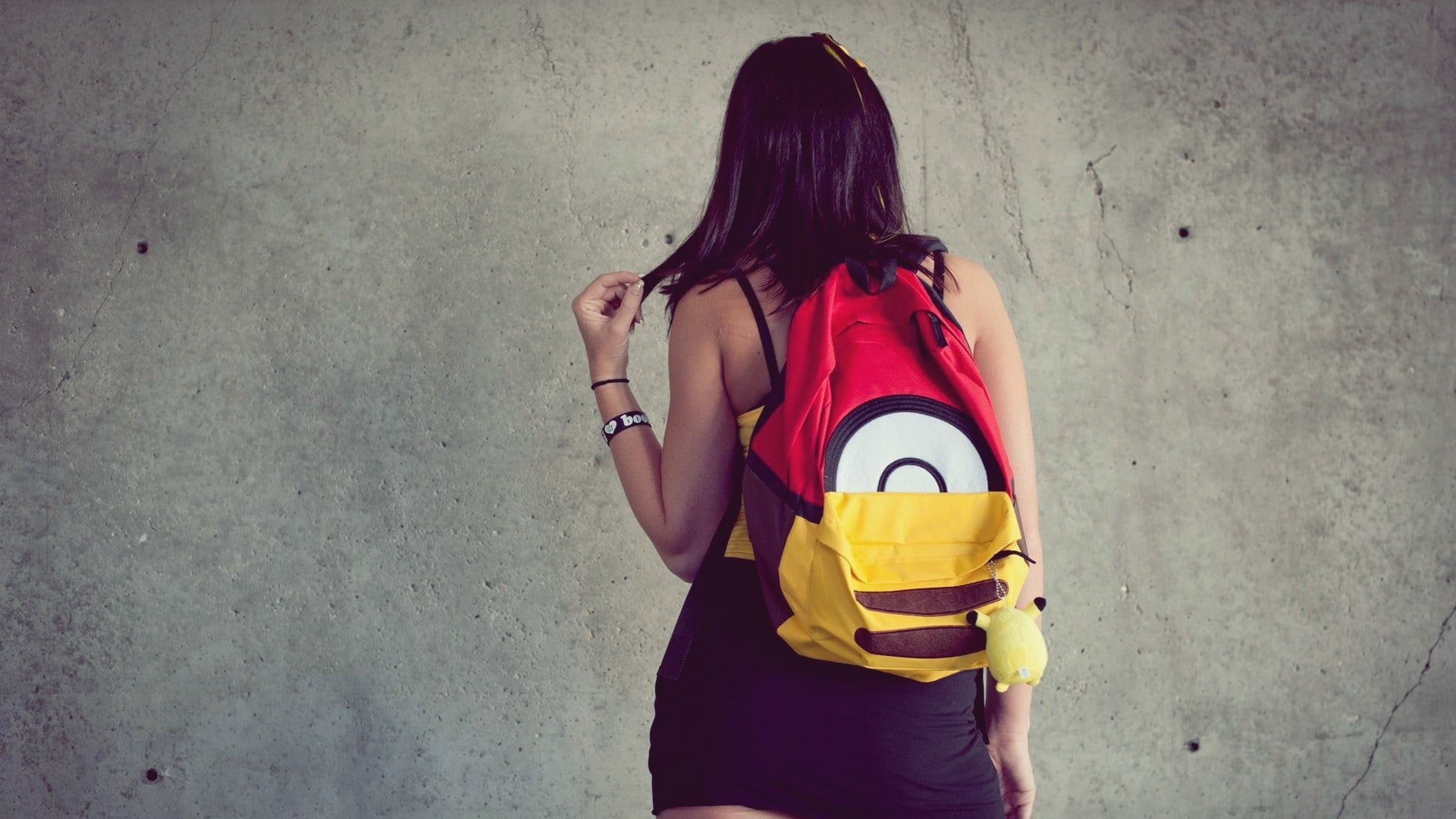 girl wearing yellow and red backpack while facing on the wall