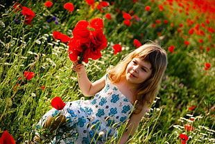 girl holding red petaled flower on green grass field