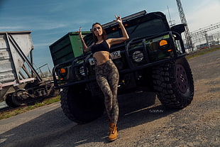 woman wearing black sports bra and green camouflage leggings standing near black vehicle at daytime