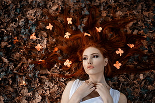 brown haired woman in white top lying on brown maple leaves