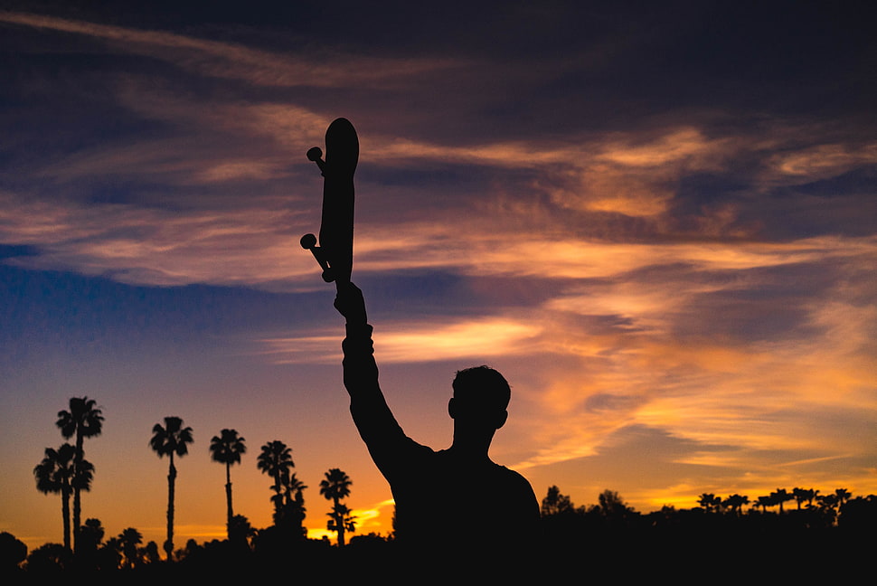 silhouette of man raising skateboard during golden hour time HD wallpaper
