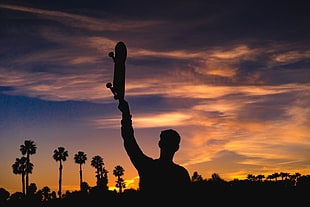 silhouette of man raising skateboard during golden hour time