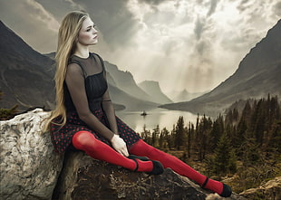 woman in black illusion neckline long sleeved long dress sitting on rock with mountain and lake in the background